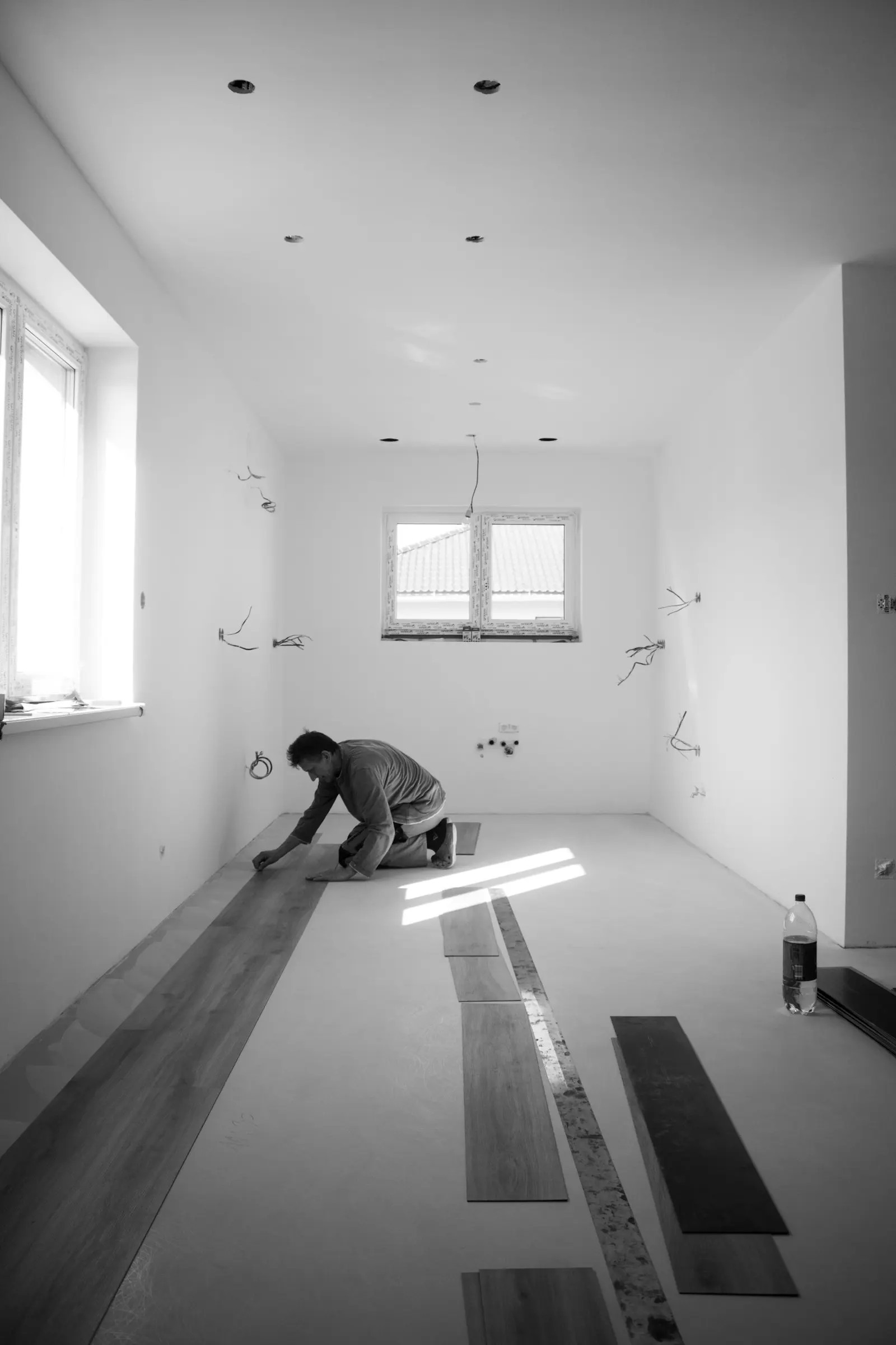 Installer laying engineered hardwood planks in an empty room during installation